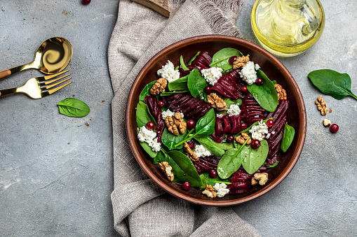 Beet or beetroot salad with baby spinach, cheese, nuts, cranberries on plate with fork, dressing and spices on gray background, top view. place for text.