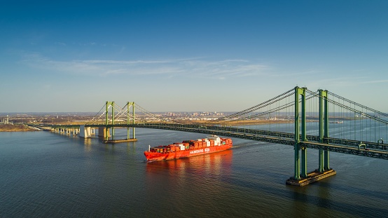 New Castle, United States – November 20, 2021: An aerial view of a cargo ship under Delaware Memorial bridge in New Castle, America