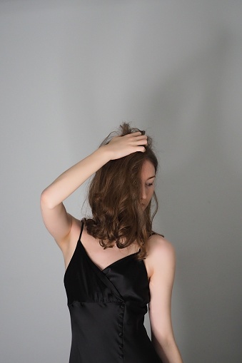 A vertical shot of Caucasian brunette in simple black dress posing against gray wall background