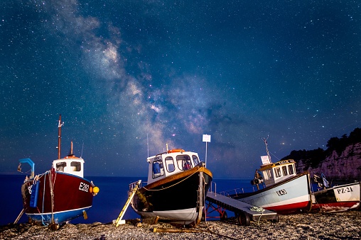 Devon, United Kingdom – November 21, 2022: The Beer beach with fishing boats on the coast under the Milkyway core