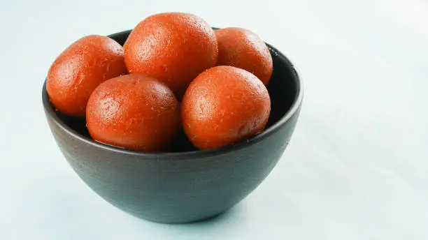 Photo of Sweet Gulab Jamun served in black ceramic bowl, Famous Indian dessert sweets isolated over blue indoor studio background