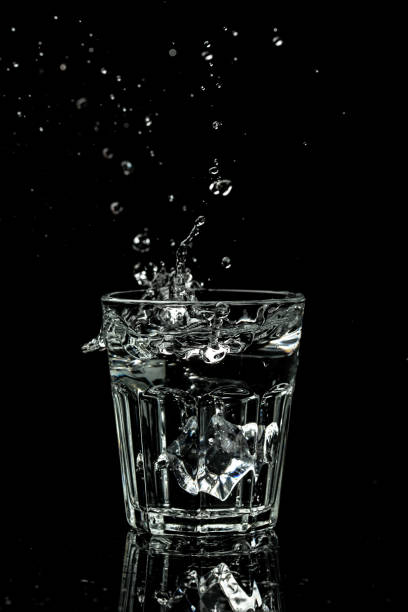vista ravvicinata dei cubetti di ghiaccio che spruzzano nell'acqua sono isolati su uno sfondo nero. immagine verticale, luogo per il testo - martini brand vermouth foto e immagini stock