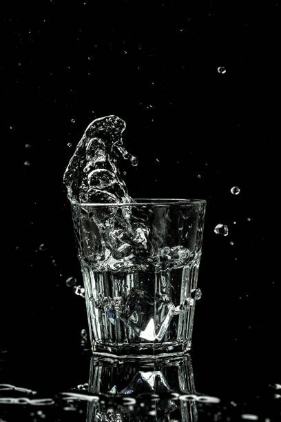 spruzzi e gocce d'acqua in un bicchiere sono isolati su uno sfondo nero. immagine verticale, luogo per il testo - martini brand vermouth foto e immagini stock