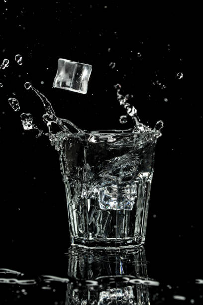 vista ravvicinata dei cubetti di ghiaccio che spruzzano nell'acqua sono isolati su uno sfondo nero. immagine verticale, luogo per il testo - martini brand vermouth foto e immagini stock