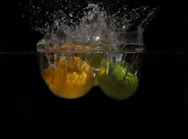 Lemon and lime splashing into the water on a black background