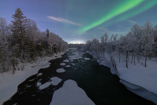 A chilling view of a frozen river and winter forest under the beautiful Aurora Borealis sky