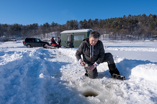 Lac Ste Marie Quebec, Canada – February 08, 2020: A female fishing on a frozen lake near a fishing hut in Lac Ste Marie, Quebec, Canada
