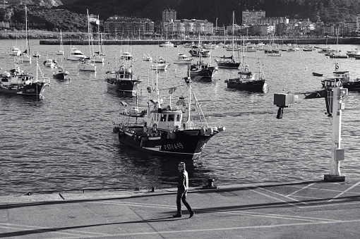 Basque Country, Spain – December 27, 2012: A grayscale wallpaper of a man walking through the port with moored boats