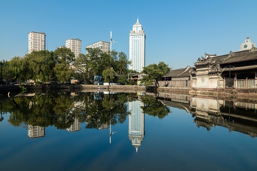 The Chengdu cityscape with water reflecting buildings and clear sunlit sky, trees around
