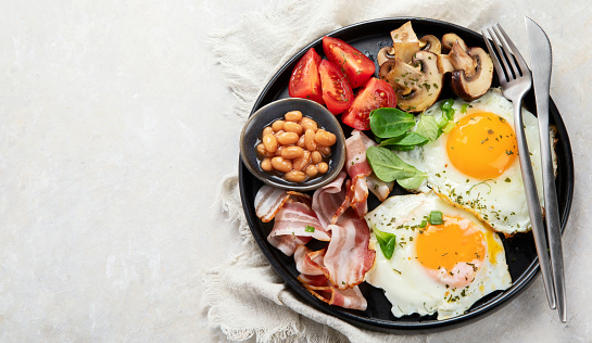 Full English breakfast with fried egg, sausage, bacon and toast on grey background. Top view, copy space