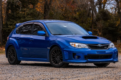 philadelphia, United States – April 11, 2022: A blue subaru wrx car parked in a dirty parking lot with fall foliage in the background