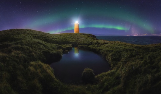 A lighthouse under a starry sky with Aurora and reflection in water in Iceland
