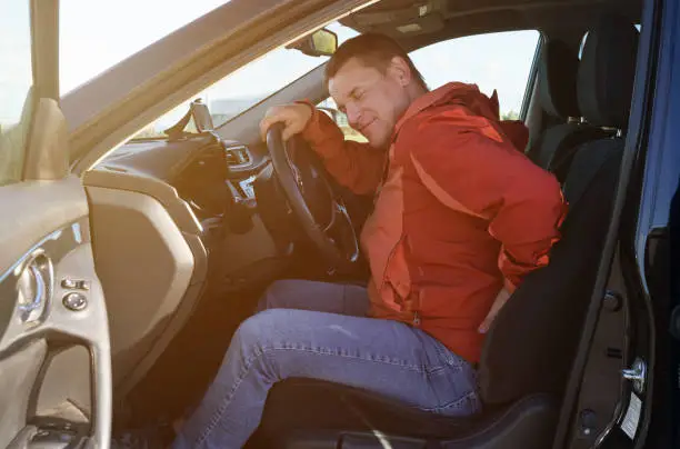 A tired driver holds on to his back, which hurts after a long drive. Security concept.