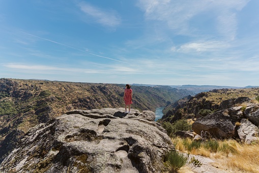 A landscape of Douro International Natural Park in Portugal, a female in a pink dress standing on high hill