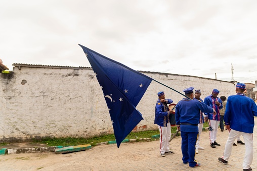 Saubara, Brazil – August 07, 2022: Members of the cultural group Encontro de Chegancas wear white and blue clothes and carry a flag. Saubara, Bahia.