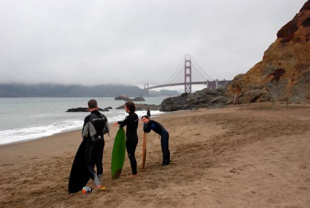 Surfers on Baker Beach in San Fransisco with Golden Gate Bridge in the background San Fransisco, United States – October 18, 2008: Three surfers on Baker Beach in San Fransisco with Golden Gate Bridge in the background baker beach stock pictures, royalty-free photos & images