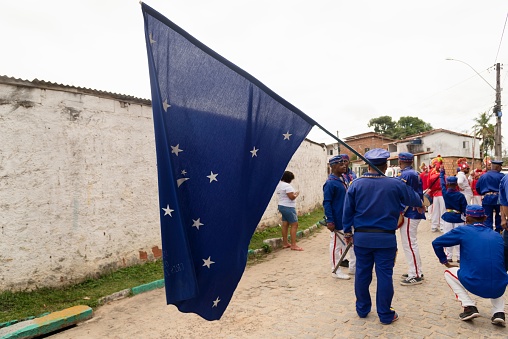Saubara, Brazil – August 07, 2022: Members of the cultural group Encontro de Chegancas wear white and blue clothes and carry a flag. Saubara, Bahia.
