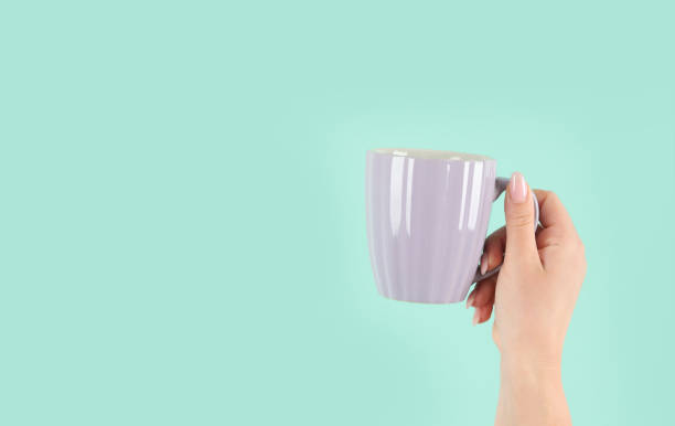 istock Arms raised up holding tea cup on green background. 1446427398