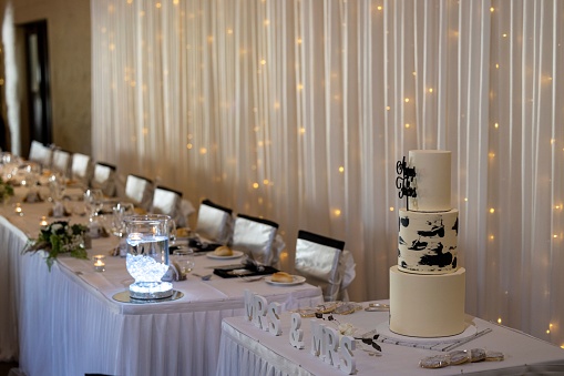 A wedding cake table and a decorated dinner table with a curtain with bokeh lights in background