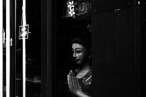 A grayscale of a Chinese-style female mannequin with praying hands displayed in a shop window