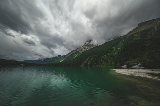 Beautiful view of mountain range covered in greenery under cloudy sky reflecting on water of emerald lake
