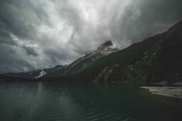 Beautiful evening view of mountain range covered in greenery under cloudy sky reflecting on water of emerald lake