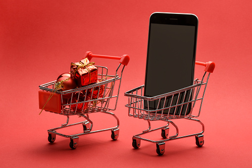 Christmas shopping. Online Christmas shopping concept. Christmas gifts and a smart phone in the shopping carts on the red background