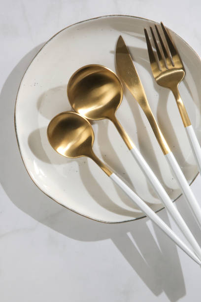 istock Matte gold flatware set with white handles, fork, spoon, knife and teaspoon on ceramic plate, top view 1446433849