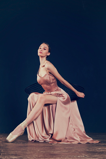 a portrait of a ballerina in a pink dress is sitting on a chair with her leg in the slit of the dress