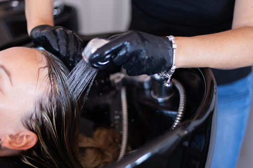 Hair stylist washing woman hair in salon. Selective focus.