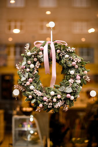 beautiful round Christmas wreath of fir branches decorated with pink glitter balls and pink dry flowers and bow hanging on glass showcase
