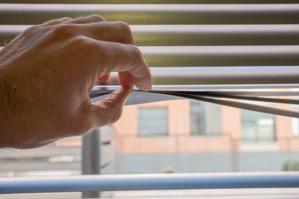 istock Man's hand revealing white venetian blinds. Looking out hidden 1446438747