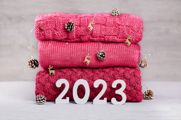 wooden numbers 2023, a stack of knitted sweaters in fashionable viva magenta color, a garland in the form of pine cones. happy new year. - viva magenta 個照片及圖片檔