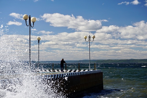 The pier looks out to sea in sunny cloudy weather. Beautiful pier with lamps in summer weather. Bright blue sky with clouds over the pier in Vladivostok.