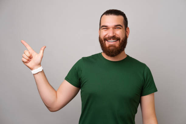 Smiling bearded man is pointing aside at the copy space for your text. stock photo