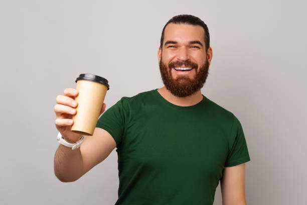 Wide smiling hipster man is giving you a fresh take away cup of coffee. stock photo