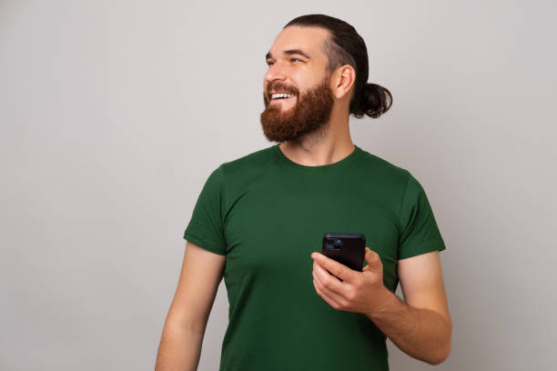 istock Smiling bearded man is holding his phone and looking up at the copy space. 1446447430