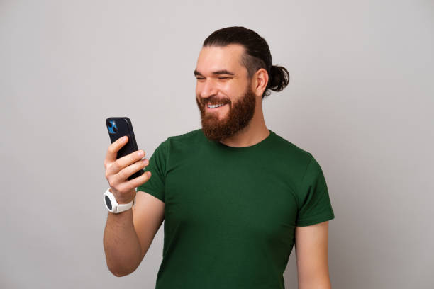 Happy bearded man is holding his phone and looking at it while misling. stock photo