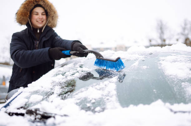 istock Young man cleaning snow from car with brush. 1446448644