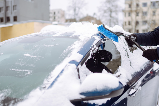 Young man cleaning snow from car with brush. Transport, winter, weather, people and vehicle concept.