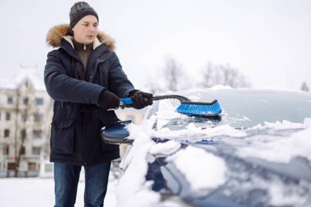 istock Young man cleaning snow from car with brush. 1446448648