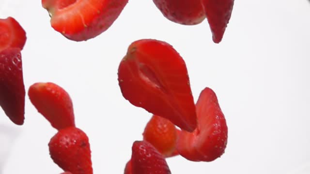 Close-up of sweet red strawberry slices falling diagonally on a white background