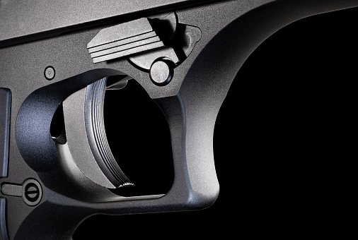 Trigger for a large and metal framed semi automatic handgun that is on a black background.