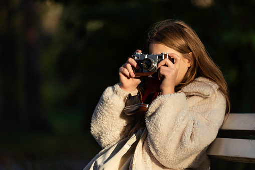 A teenage girl taking photos with an old camera in the park