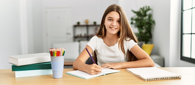 Adorable girl doing homework sitting on table at home