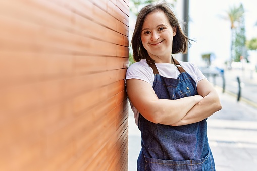 Young down syndrome woman smiling confident wearing apron at street