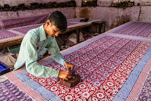 Young man working in block printing factory in Jaipur, India, Jaipur is famous for a screen and block printing. Block printing is the process of printing patterns by means of engraved wooden blocks.