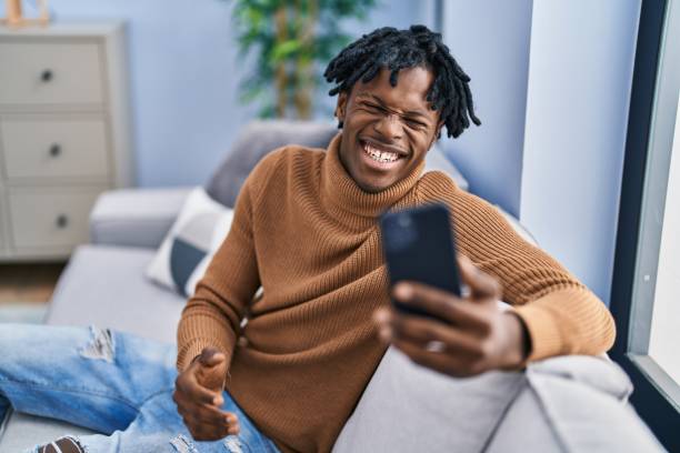 istock Young african man with dreadlocks using smartphone doing video call celebrating achievement with happy smile and winner expression with raised hand 1446459526