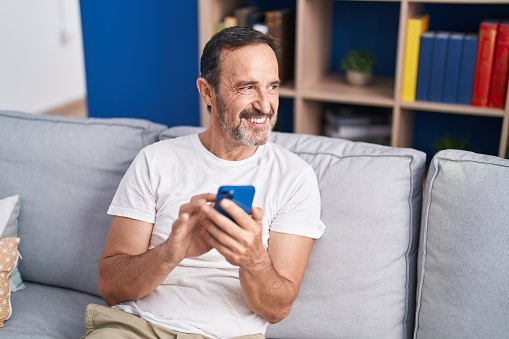 Middle age man using smartphone sitting on sofa at home