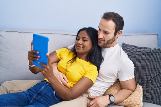 istock Man and woman interracial couple using touchpad lying on sofa at home 1446459763